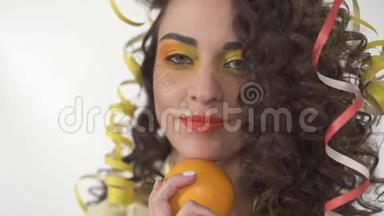 特写年轻<strong>俏皮</strong>的微笑女孩与明亮的化妆抱着橙色的肖像。 慢动作。